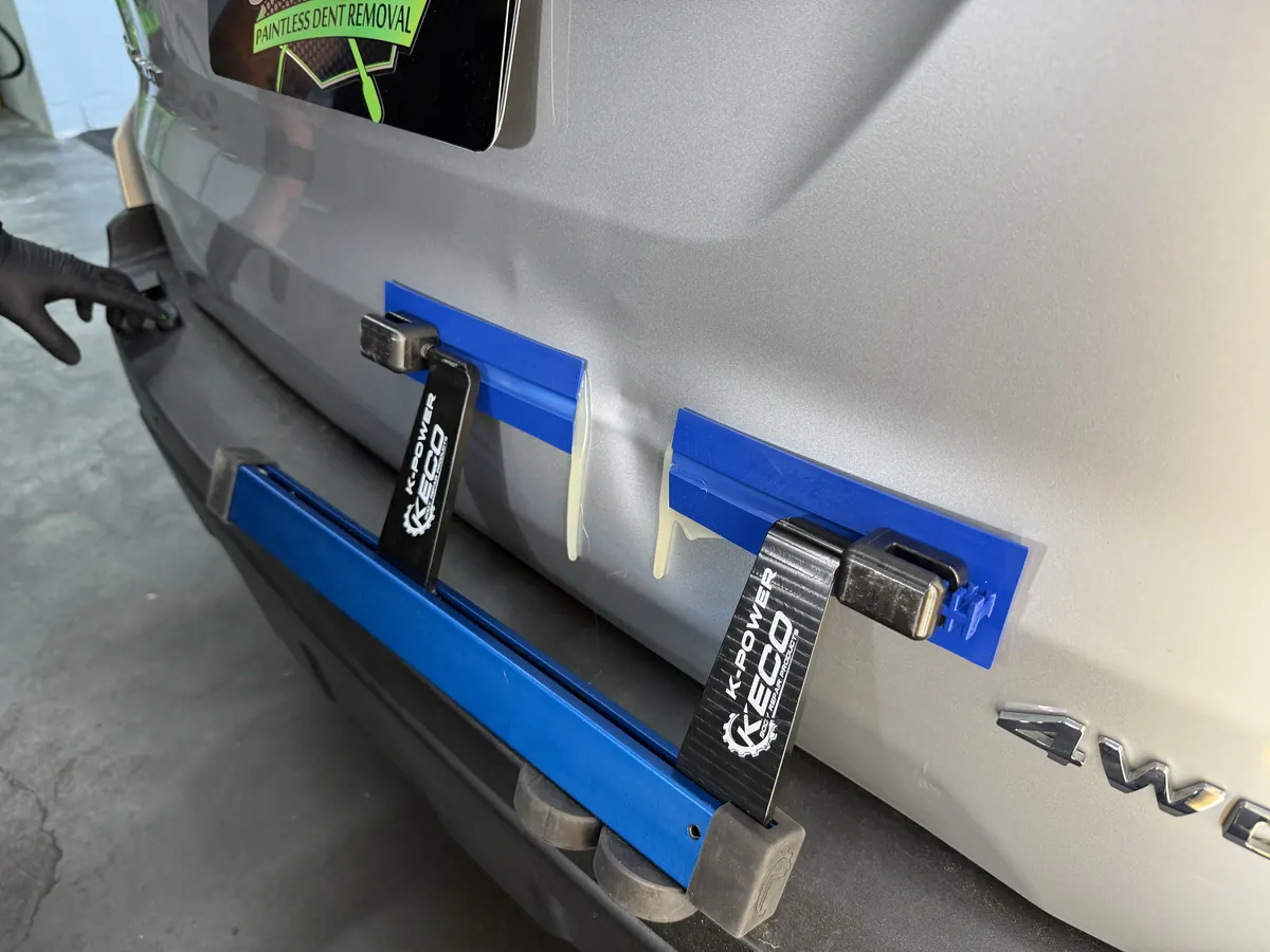 Glue-pull tabs and a lifting bar set on a tailgate for paintless dent repair