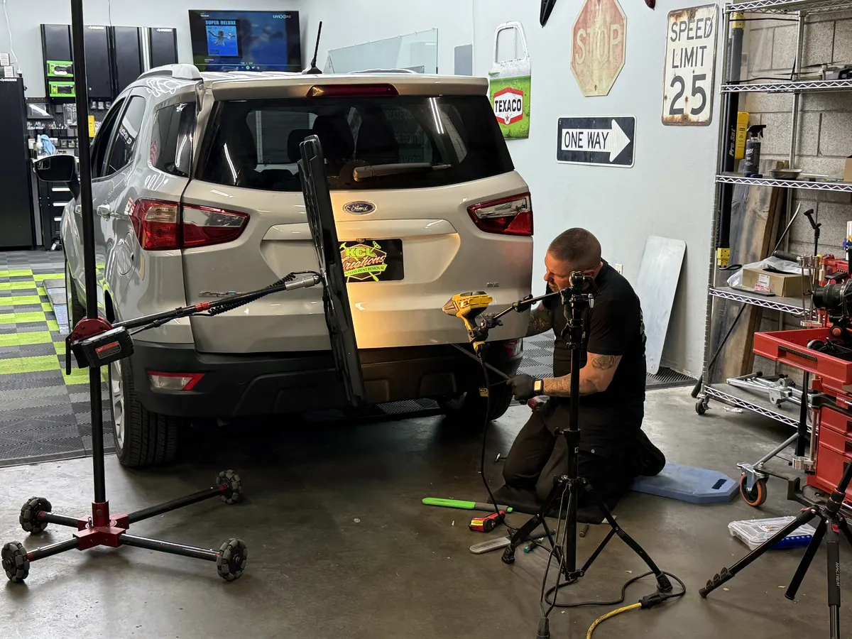 KCL technician working a lift-gate dent in the Loveland shop with PDR lights and tools