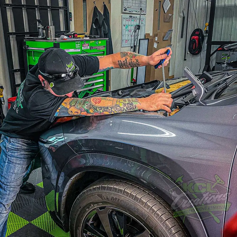 KCL Creations technician working a fender dent in the Loveland shop, KCL green toolbox behind