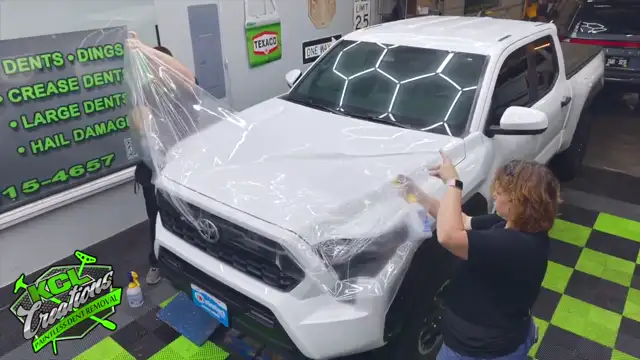 Crystal and Hayden installing Xpel paint protection film on a white Toyota Tacoma at KCL Creations in Loveland